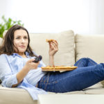 femme grignotant à la maison devant la télé dans son canapé