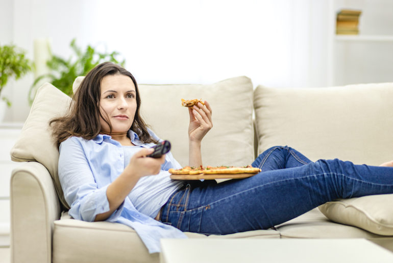 femme grignotant à la maison devant la télé dans son canapé