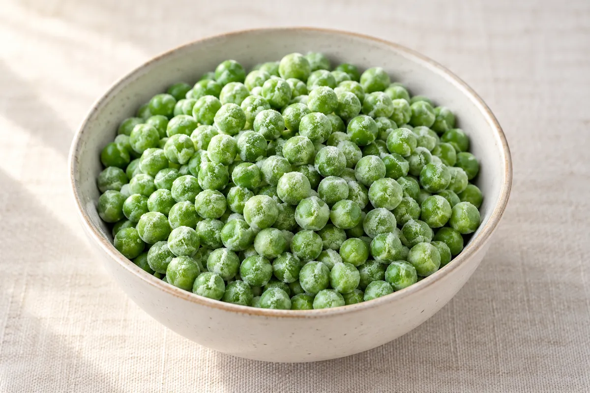 Petits pois surgelés crus sur un fond de lin clair.